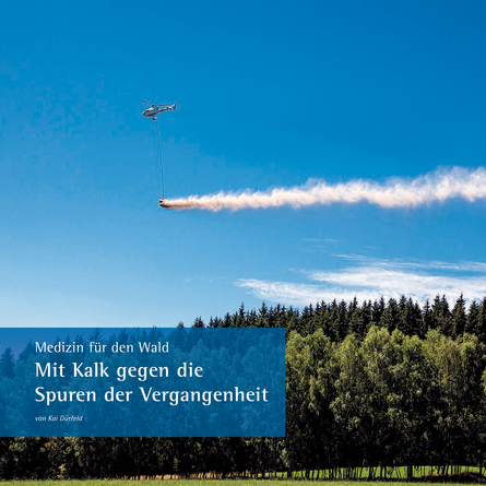 Ein Hubschrauber fliegt über ein Waldgebiet und wirft aus einem angehängten Behälter Kalk ab.