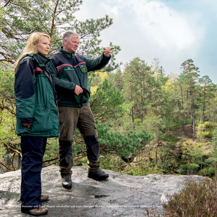 Zwei Sachsenforst-Mitarbeiter stehen auf einem Felsen und blicken in die Landschaft.