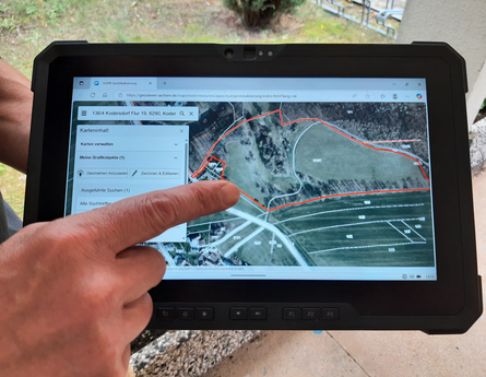 Großaufnahme eines Fingers, der auf ein Touchpad zeigt, auf dem eine Luftbildkarte zu sehen ist.
