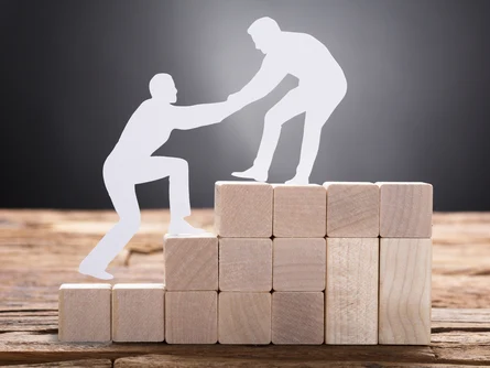 Zwei Figuren helfen sich beim Besteigen eines Holzstapels