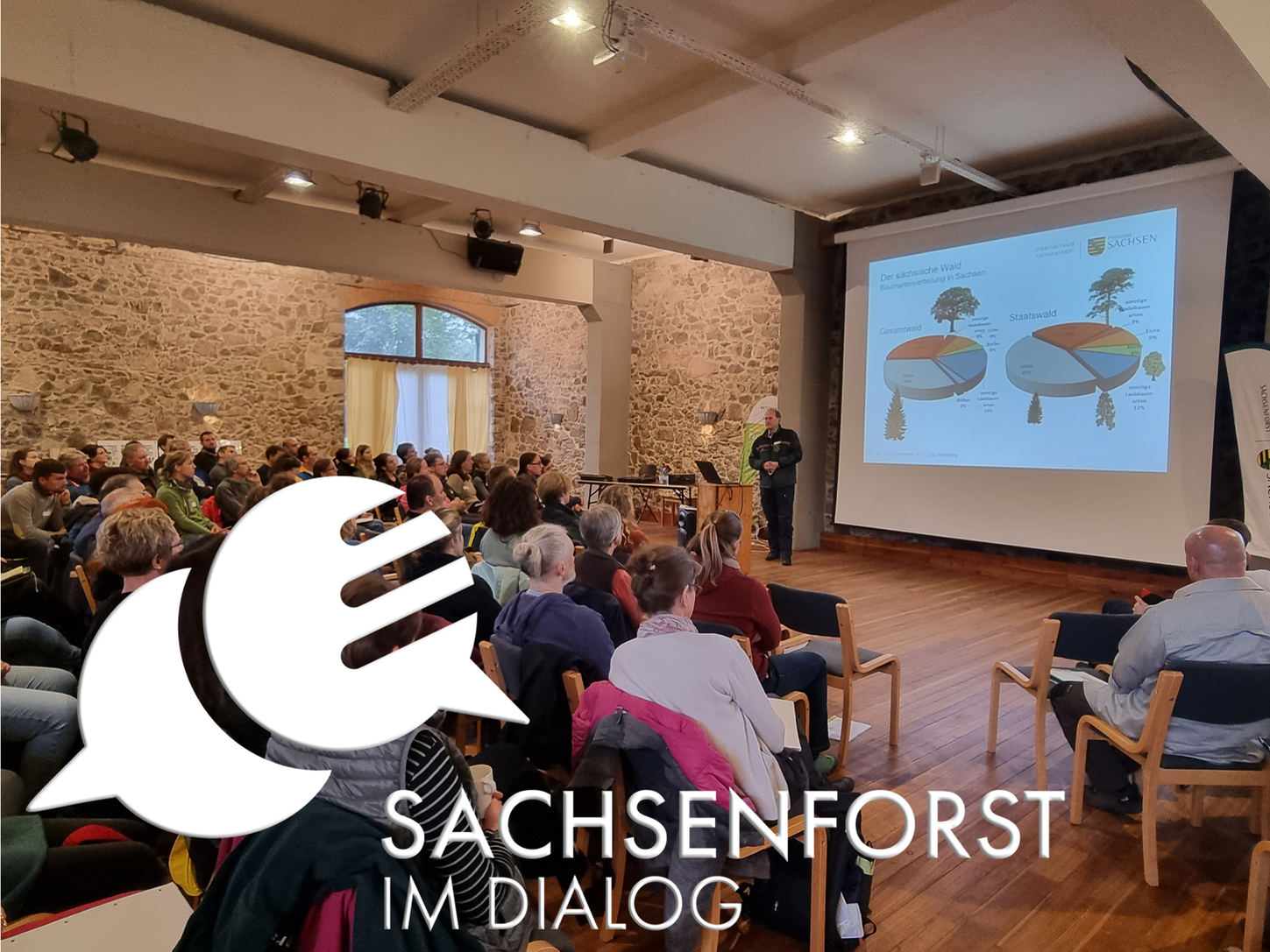 Blick in einen Vortragsraum mit weißem Logo von Sachsenforst im Dialog