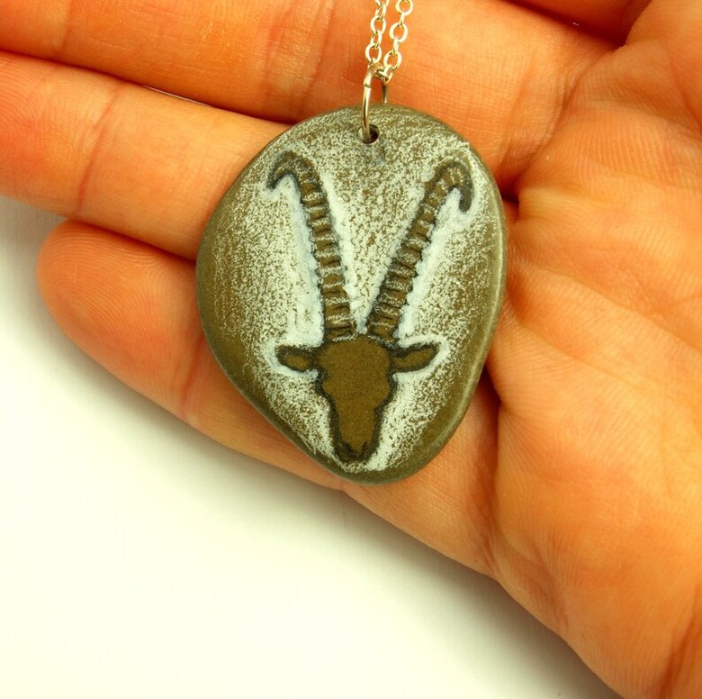 Kette mit Steinanhänger und Tierkopf liegt in einer Hand