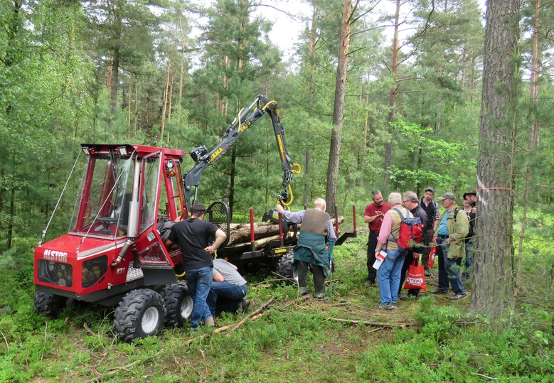 Mehreren Personen im Wald wird die Arbeitsweise eines Forwarders erl&auml;utert.