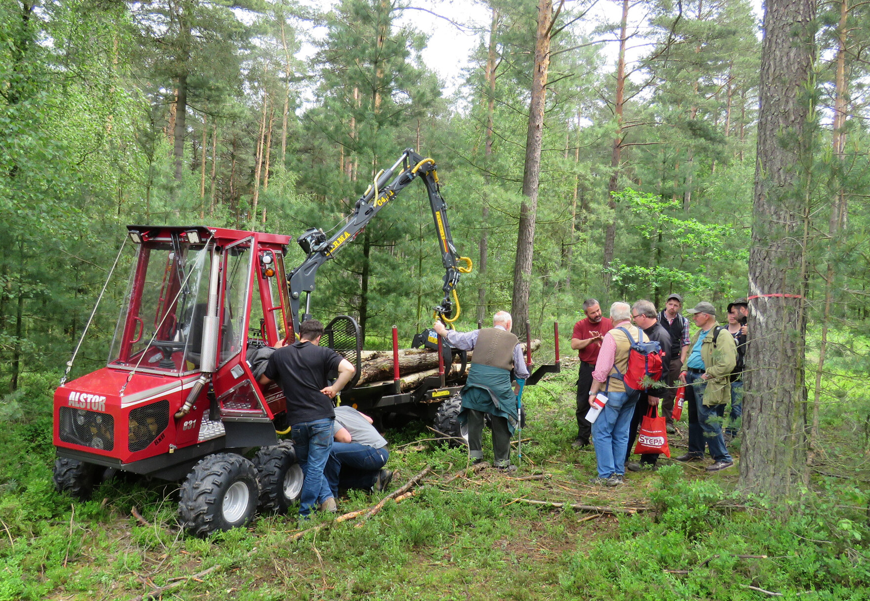 Mehreren Personen im Wald wird die Arbeitsweise eines Forwarders erläutert.