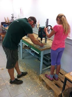 Ein Mitarbeiter des Waldschulheimes mit einem Mädchen an einer Bohrmaschine.