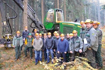 Die Delegation steht im Wald vor einem Harvester