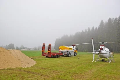 Auf einem Feld stehen neben einem Kalkhaufen der Transporter f&uuml;r den Helikopter und der Helikopter.