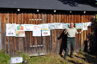 Stephan Schusser vor einer Holzhütte, an deren Wand mehrere Poster angebracht sind.