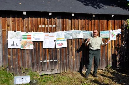 Stephan Schusser vor einer Holzh&uuml;tte, an deren Wand mehrere Poster angebracht sind.