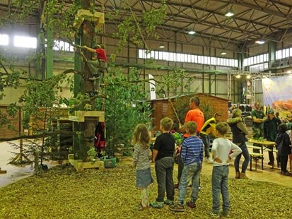 Ein Kind klettert, gesichert von einem Mitarbeiter, während weitere Kinder warten.