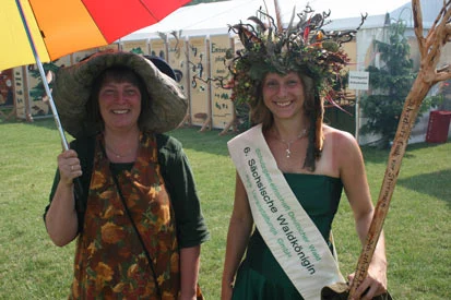Die S&auml;chsische Waldk&ouml;nigin Saskia I. (rechts) l&auml;chelnd an der Seite einer Frau mit Hut und Schirm