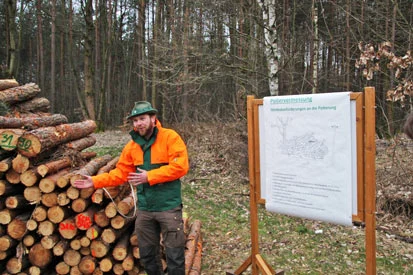 Stefan M&uuml;ller vor einem Holzstapel und einer Pr&auml;sentationstafel.