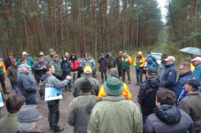 Herr Stahn steht im Wald auf einer Wegkreuzung inmitten der Tagungsteilnehmer