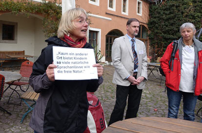 Gisela Stöckmann halt ein Schild, auf dem steht: Kaum ein anderer Ort bietet Kindern so viele natürliche Sprachanlässe wie die freie Natur.