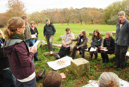 Teilnehmer des Workshops "Kleine Waldphilosophen" in einer Gesprächsrunde auf Holzbänken auf einer Wiese