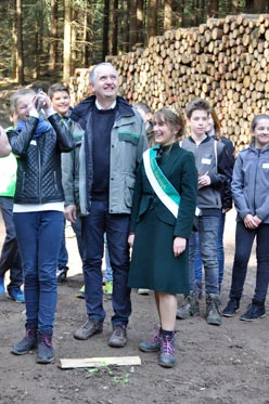 Eine Sch&uuml;lerin misst mit einem Baumh&ouml;henmesser, der Minister und die Waldk&ouml;nigin schauen lachend zu