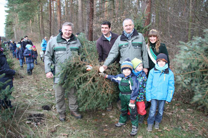 Andreas Padberg, Landrat Henry Graichen, Staatsminister Thomas Schmidt und die Waldkönigin präsentieren mit drei Kindern den frisch gefällten Weihnachtsbaum.